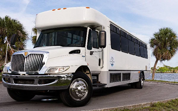 A white 32-passenger shuttle bus with the Performance logo parked near a waterfront with palm trees.