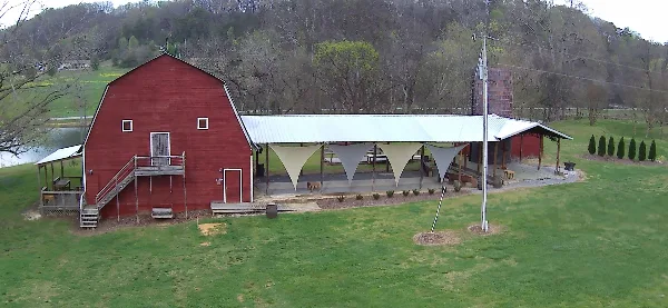 Aerial view of a red rustic barn wedding venue with a covered reception area and grassy grounds.