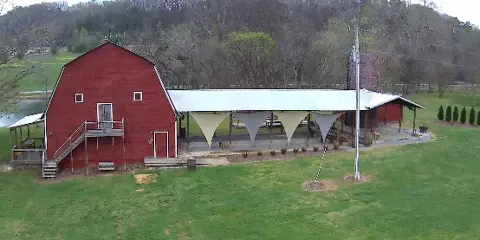 Aerial view of a red rustic barn wedding venue with a covered reception area and grassy grounds.