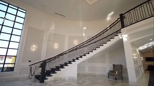 Interior view of a grand event venue featuring a curved staircase, white paneled walls, and marble flooring.