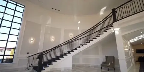 Interior view of a grand event venue featuring a curved staircase, white paneled walls, and marble flooring.