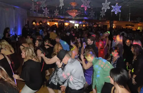 A large group of people dancing at a special event under colorful lighting and snowflake decorations.