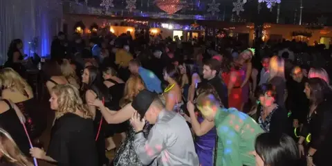 A large group of people dancing at a special event under colorful lighting and snowflake decorations.