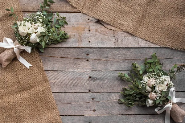 Two white rose bouquets with greenery and burlap wraps resting on a rustic wooden table.