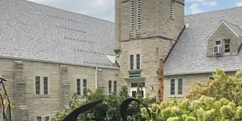 Exterior view of the historic stone building of Art Sanctuary of Indiana with a tower and slate roof.