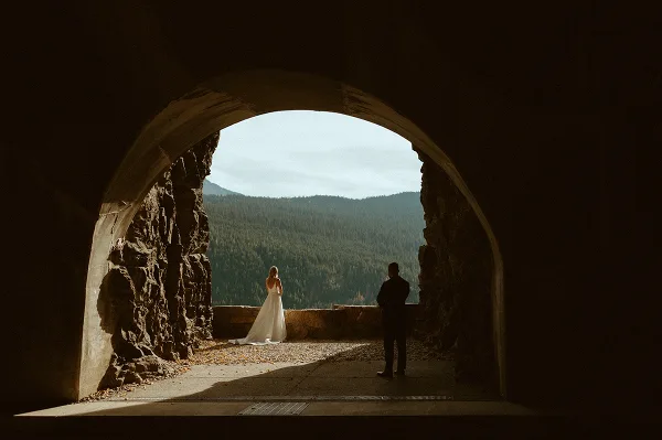 A bride and groom standing in a stone archway overlooking a forested mountain valley.