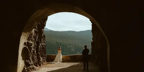 A bride and groom standing in a stone archway overlooking a forested mountain valley.