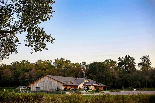 Exterior view of a large wooden barn-style event center with a windmill and outdoor grounds.