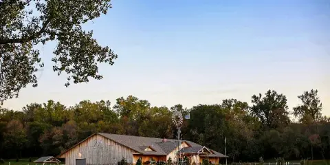 Exterior view of a large wooden barn-style event center with a windmill and outdoor grounds.