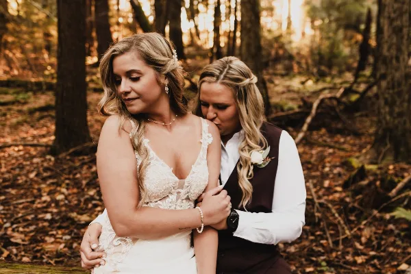 A professional wedding photograph of a couple embracing in a forest setting.