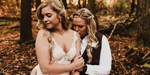 A professional wedding photograph of a couple embracing in a forest setting.