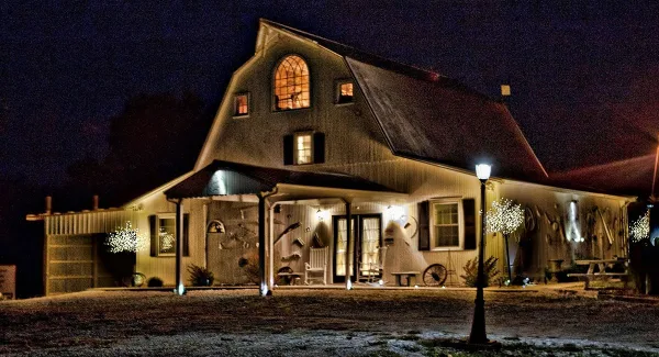 A nighttime exterior view of a large, rustic wooden lodge with a gambrel roof, illuminated windows, and a covered porch.