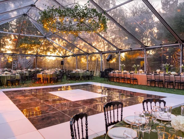 A large clear-frame event tent set up outdoors with a dance floor and dining tables.