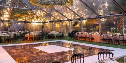 A large clear-frame event tent set up outdoors with a dance floor and dining tables.