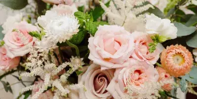 A close-up of a bride in a white dress holding a lush wedding bouquet with pink and white roses, white chrysanthemums, and greenery.