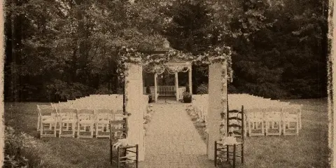 Outdoor wedding ceremony setup featuring a floral arch, rows of white chairs, and a gazebo in a garden setting.