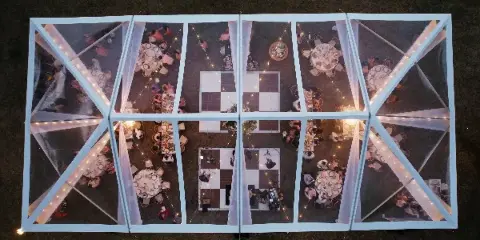 Aerial view of a clear-frame event tent with string lighting, round dining tables, and a checkered dance floor.