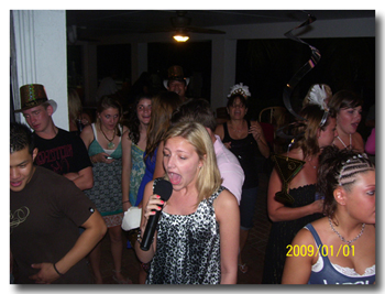 A woman singing into a microphone at a crowded indoor party event.