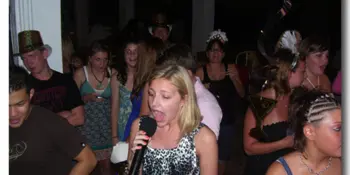 A woman singing into a microphone at a crowded indoor party event.