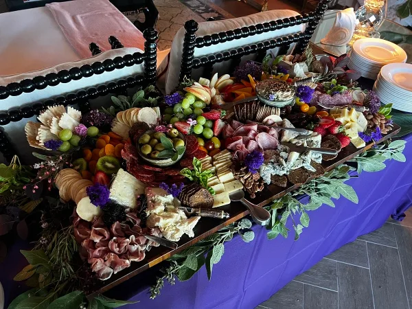 A large catering platter featuring assorted cheeses, cured meats, fruit, and decorative garnishes arranged on a table.