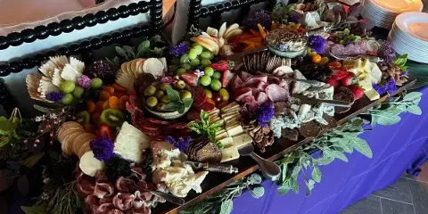 A large catering platter featuring assorted cheeses, cured meats, fruit, and decorative garnishes arranged on a table.