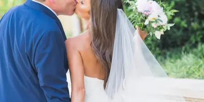 A bride and groom sharing a kiss outdoors, with the bride holding a bouquet of flowers.