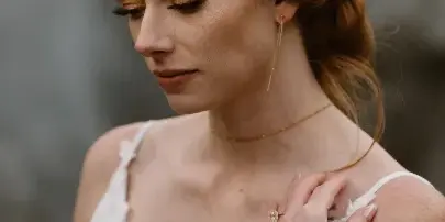 A bride with red hair styled in an updo with a floral accessory, wearing a white lace wedding dress and professional makeup.