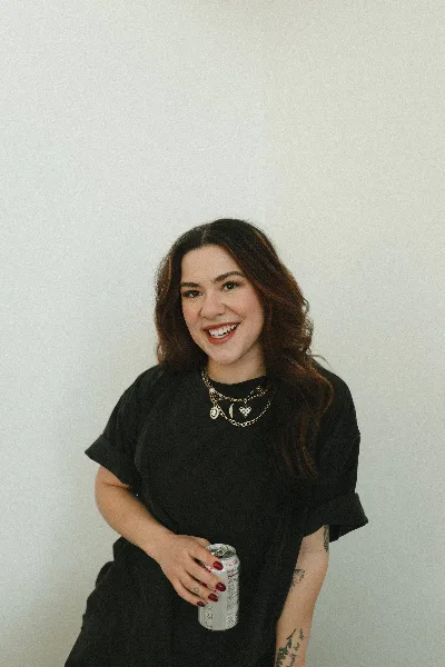 Portrait of a smiling woman with long dark hair wearing a black t-shirt and holding a beverage can.