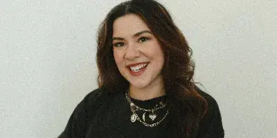 Portrait of a smiling woman with long dark hair wearing a black t-shirt and holding a beverage can.