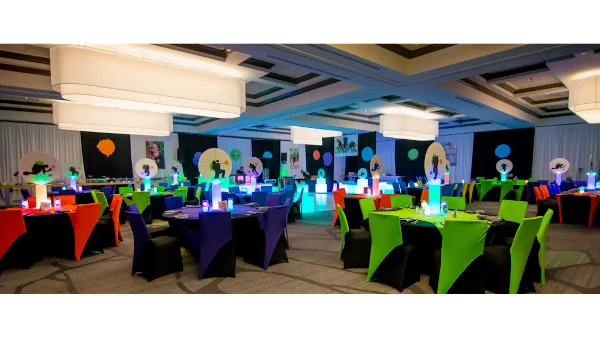 A large event hall set up with round tables, colorful chair covers, and decorative lighting.