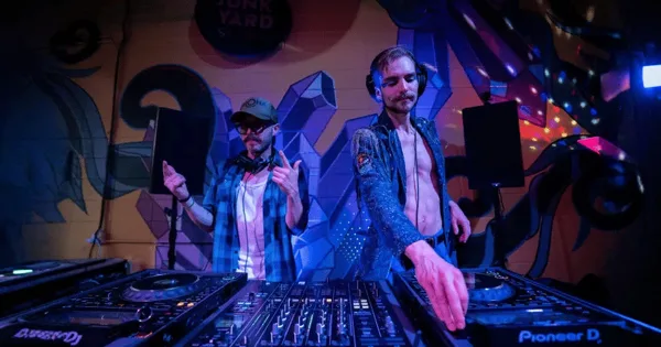 Two DJs performing at a live event with Pioneer DJ equipment and stage lighting.