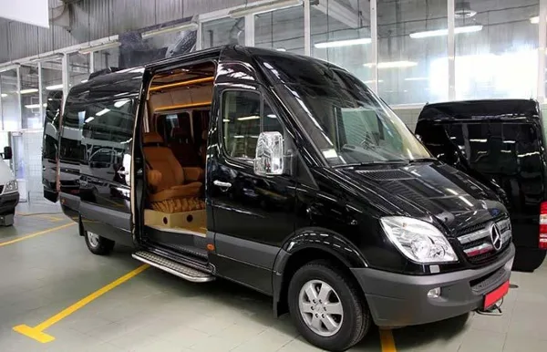 A black Mercedes Sprinter van with sliding door open, revealing a tan leather interior, parked in a garage.