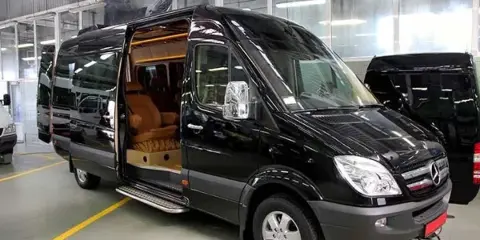 A black Mercedes Sprinter van with sliding door open, revealing a tan leather interior, parked in a garage.