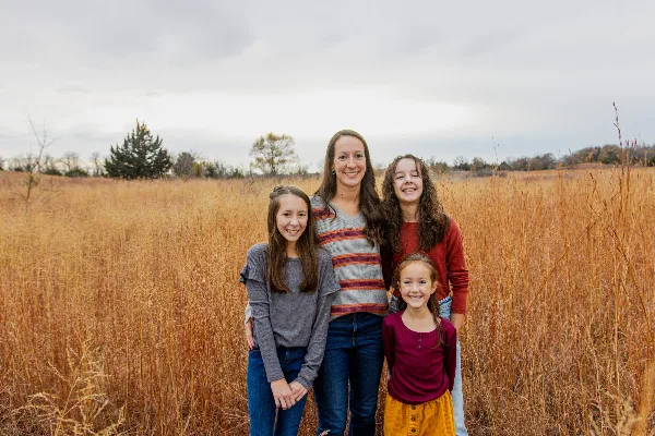A family of four standing together in a field of tall, dry grass.