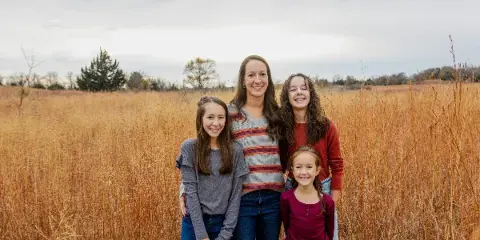 A family of four standing together in a field of tall, dry grass.