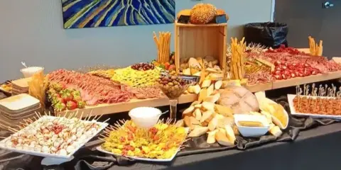 A catering buffet table displaying a charcuterie board, breads, and assorted appetizers.