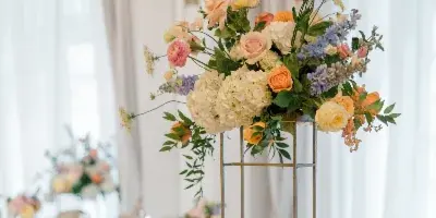 A tall floral centerpiece featuring pink, yellow, and white flowers on a gold stand, set on a decorated wedding table.