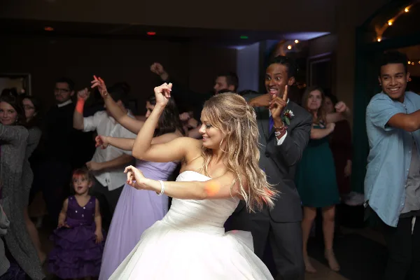 A bride and groom dancing at a wedding reception with guests in the background.