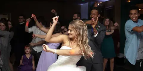 A bride and groom dancing at a wedding reception with guests in the background.