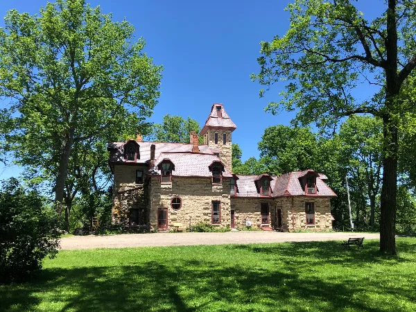 Exterior view of a historic stone castle with a tower and red roof surrounded by green trees and a lawn.