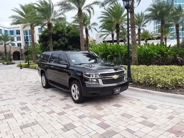 A black Chevrolet Suburban parked on a paved driveway in front of a resort-style building with palm trees.