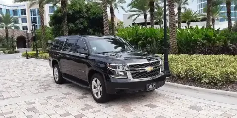 A black Chevrolet Suburban parked on a paved driveway in front of a resort-style building with palm trees.