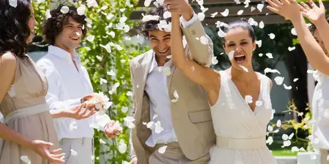 A bride and groom smiling and celebrating with guests while white flower petals are tossed in the air.