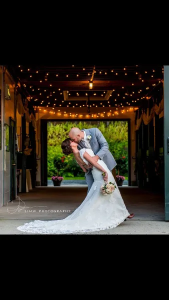 A bride and groom sharing a dip in a wedding venue decorated with string lights, with a garden visible through the open doorway.