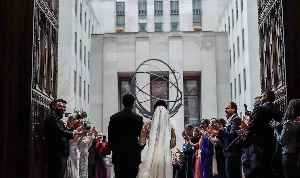 A bride and groom walking away from the camera through a line of applauding wedding guests in an urban courtyard.