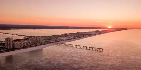 Aerial view of a coastal beach and pier at sunset
