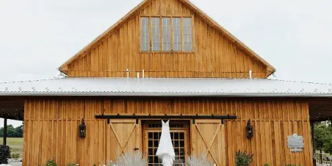 Exterior of a large wooden barn with a wedding dress hanging on the front door.