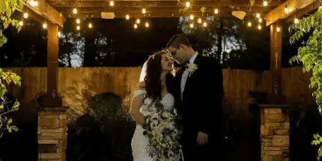 A bride and groom standing under a wooden pergola with string lights, with the Villa Borghese Caterers logo and text overlaid at the bottom.