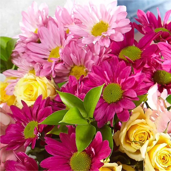 A close-up photograph of a floral bouquet featuring pink daisies, yellow roses, and green leaves.