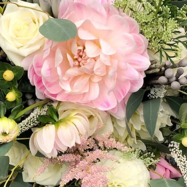 A close-up of a floral arrangement featuring a large pink dahlia, white roses, and greenery.